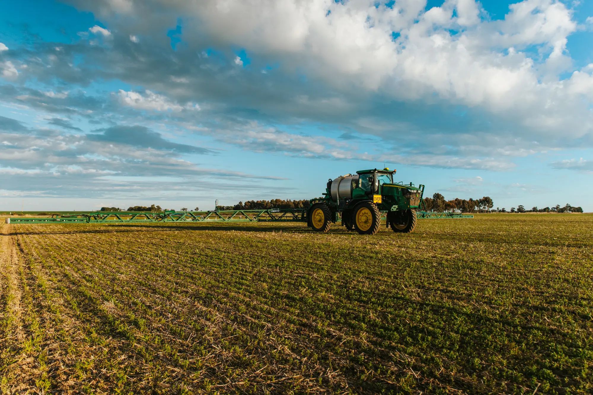 Tractor spraying crops in a field under a blue sky, promoting liquid fertiliser and healthy crops on an Australian farm.