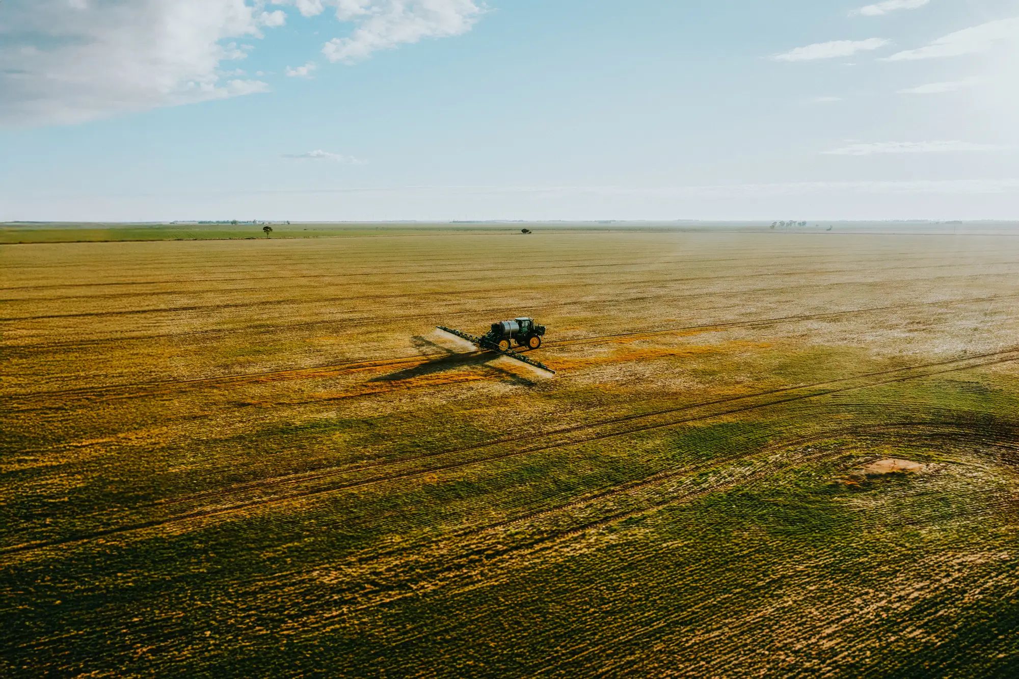 Tractor spraying crops on vast farmland, enhancing soil nutrition with liquid fertiliser for healthy crops and higher yields.